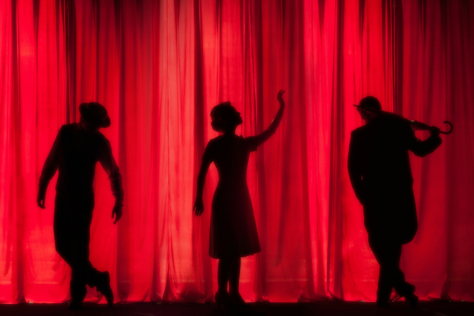 Costumed figures silhouetted against a red stage curtain